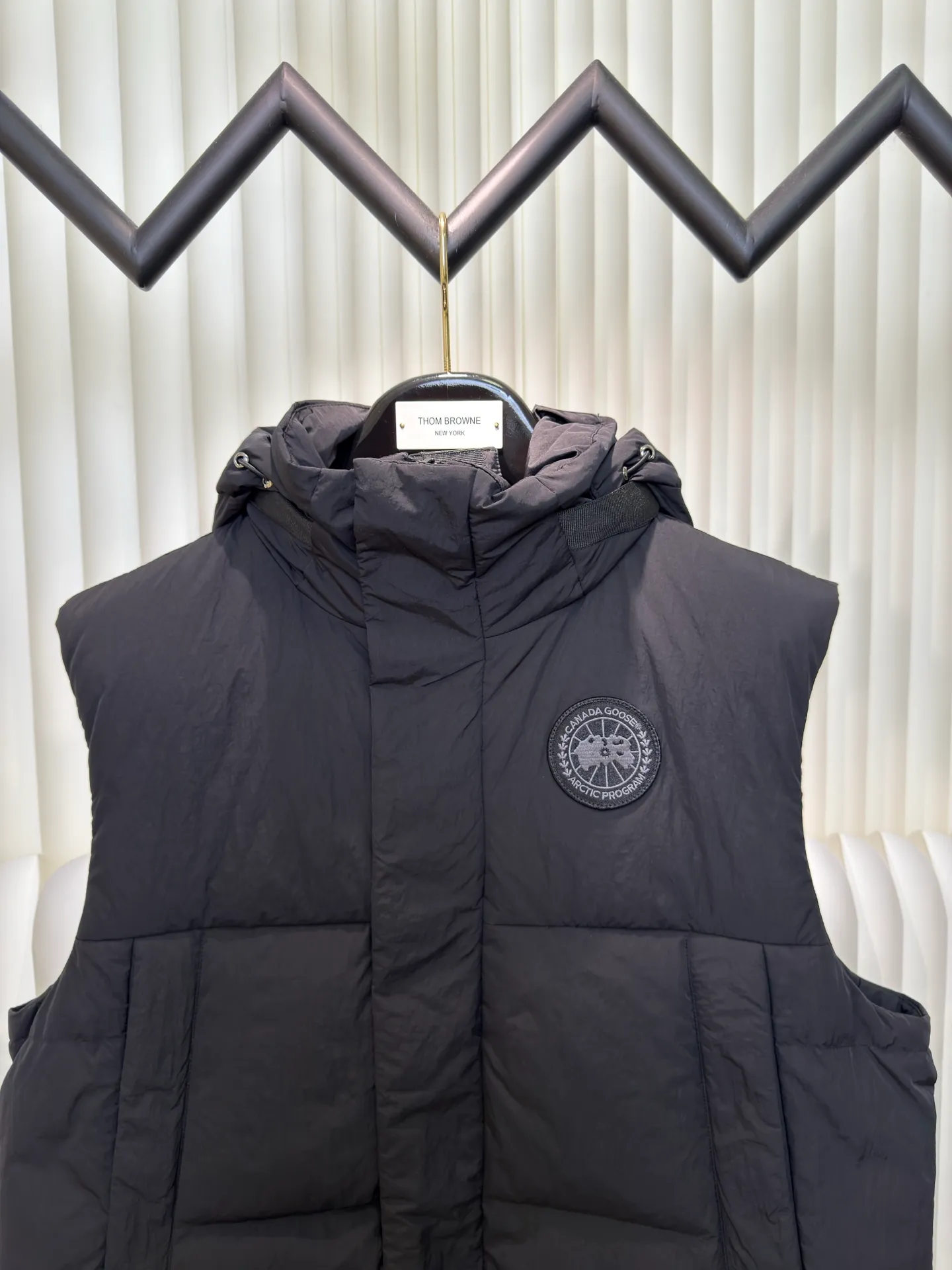 P760 Big Goose Logo Hooded Down Vest is made of high-quality protective nylon fabric, which not only enhances the wear resistance of the surface, but also takes into account wind resistance, ensuring excellent performance in various harsh weather conditions.  90 national standard high-quality white duck down: selected high-loft down, weighing 170g, light and warm, with excellent temperature locking performance and good resilience.  Three-dimensional quilting process: Precision thread reinforcement to prevent velvet drilling and ensure that the fluffy and resilient elasticity lasts as new.  Details: The ribbon is woven with polyester as the base. The brand letters are decorated on the ribbon through high-precision computer embroidery. The edges of the pattern are clear, the stitches are fine and even, and multiple layers of embroidery thread are stacked to enhance the three-dimensional effect. Size S M L XL
